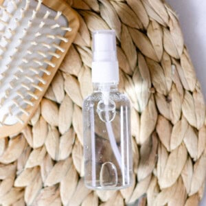 Clear spray bottle with hair growth spray on a woven bamboo mat.