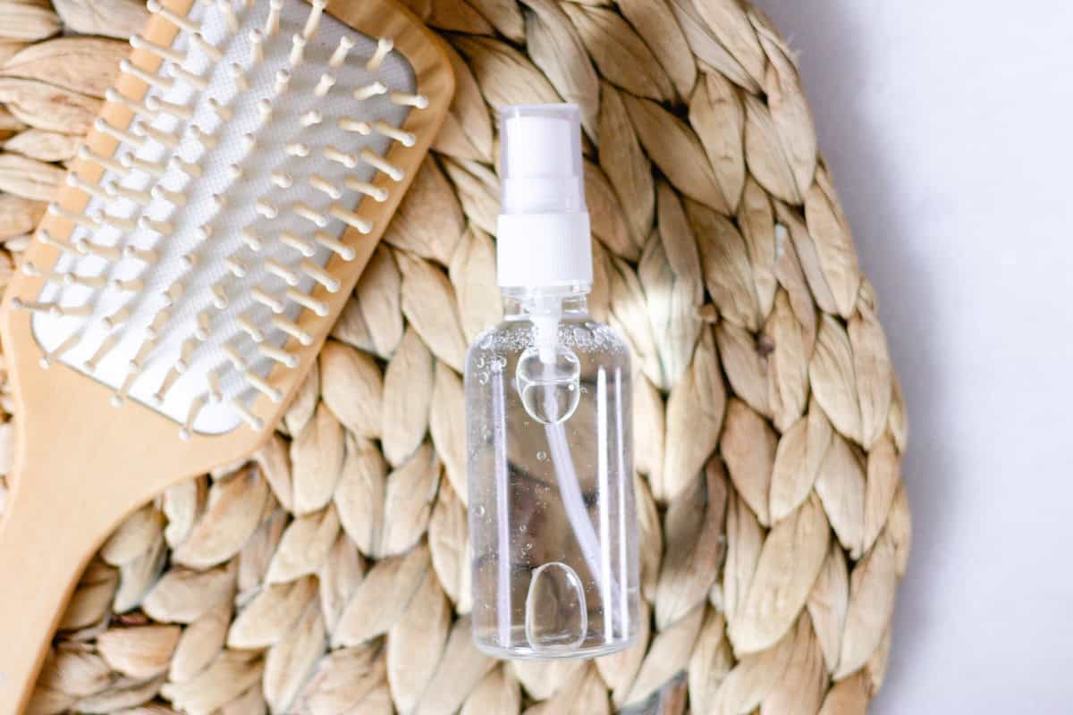 Clear spray bottle with hair growth spray on a woven bamboo mat.