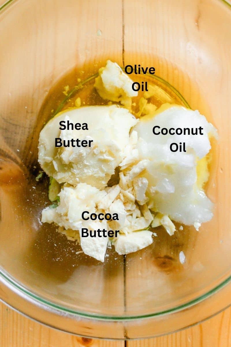 Whipped body butter ingredients in a glass bowl: shea butter, olive oil, coconut oil, and cocoa butter. 