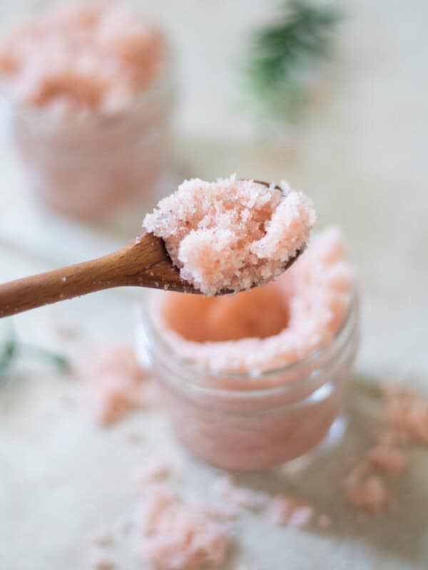 A spoonful of foot scrub being held above a jar of foot scrub.