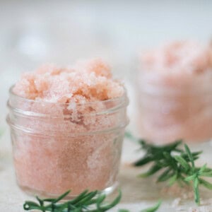 Two jars of foot scrub with fresh herbs laying around them.