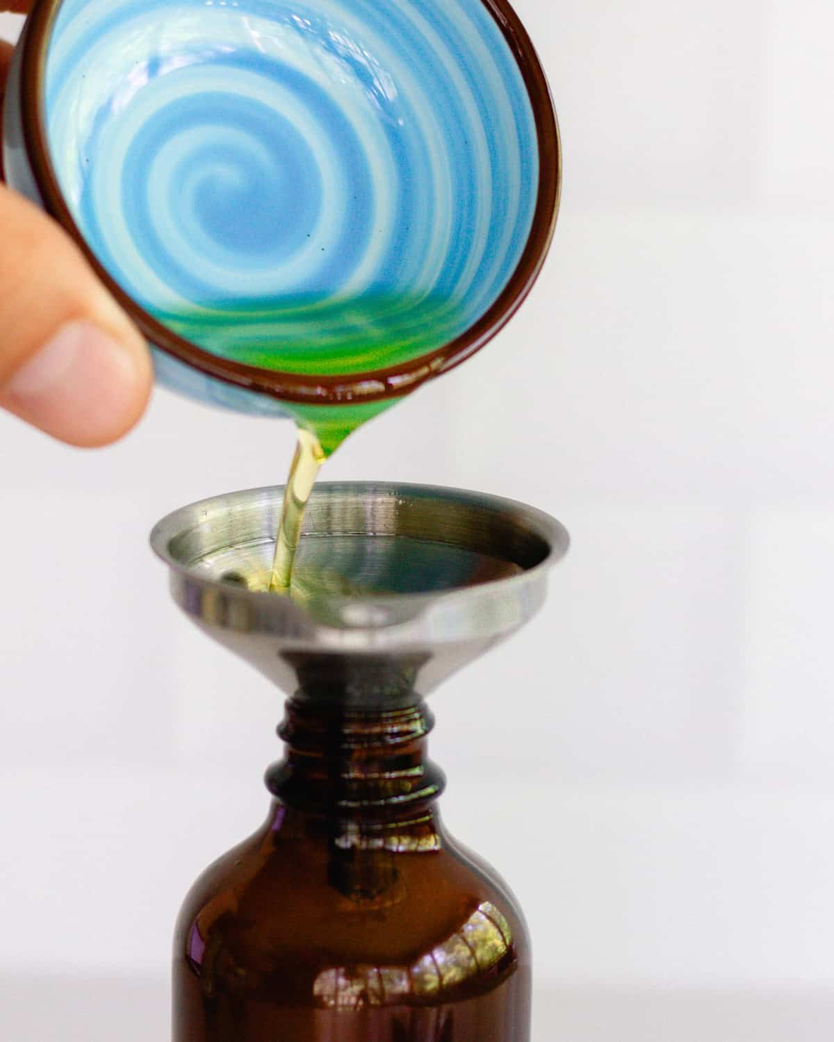 Pouring oil into an amber glass spray bottle using a metal funnel.