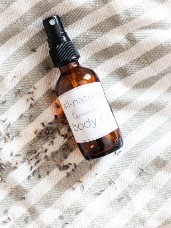 A bottle of homemade body oil laying on a striped towel with dried lavender buds.