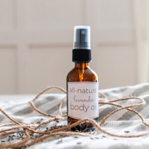 A bottle of body oil on a striped towel with twine and lavender buds.