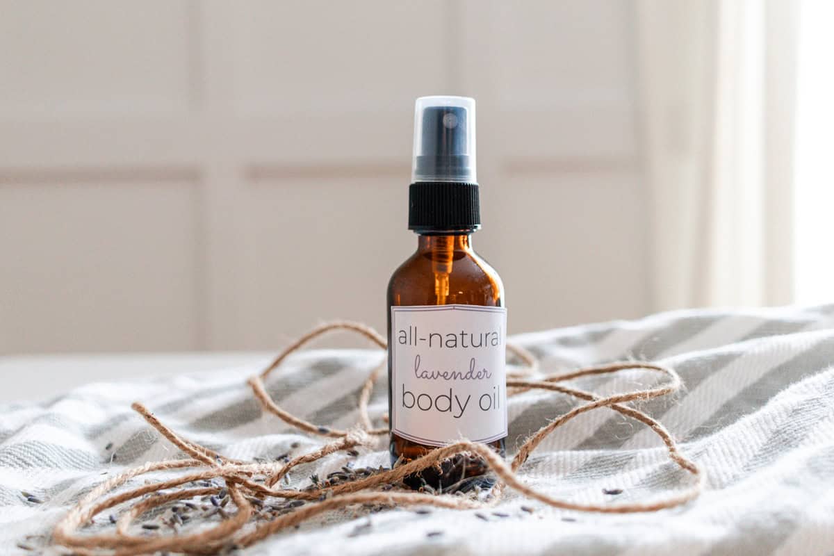 A bottle of homemade body oil sitting on a striped towel with twine and dried lavender buds.