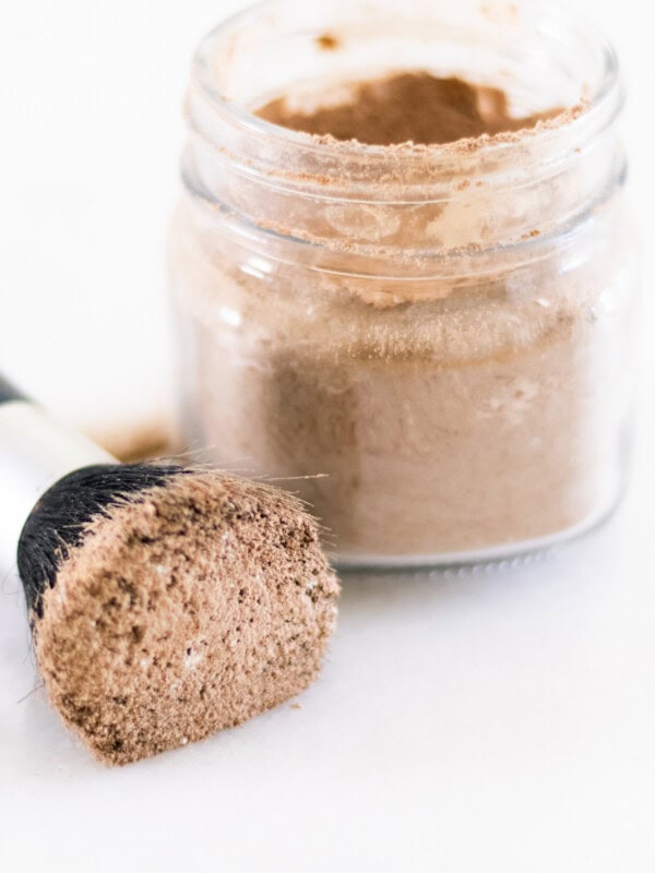 Dry shampoo on a makeup brush with a glass jar of dry shampoo sitting next to it.