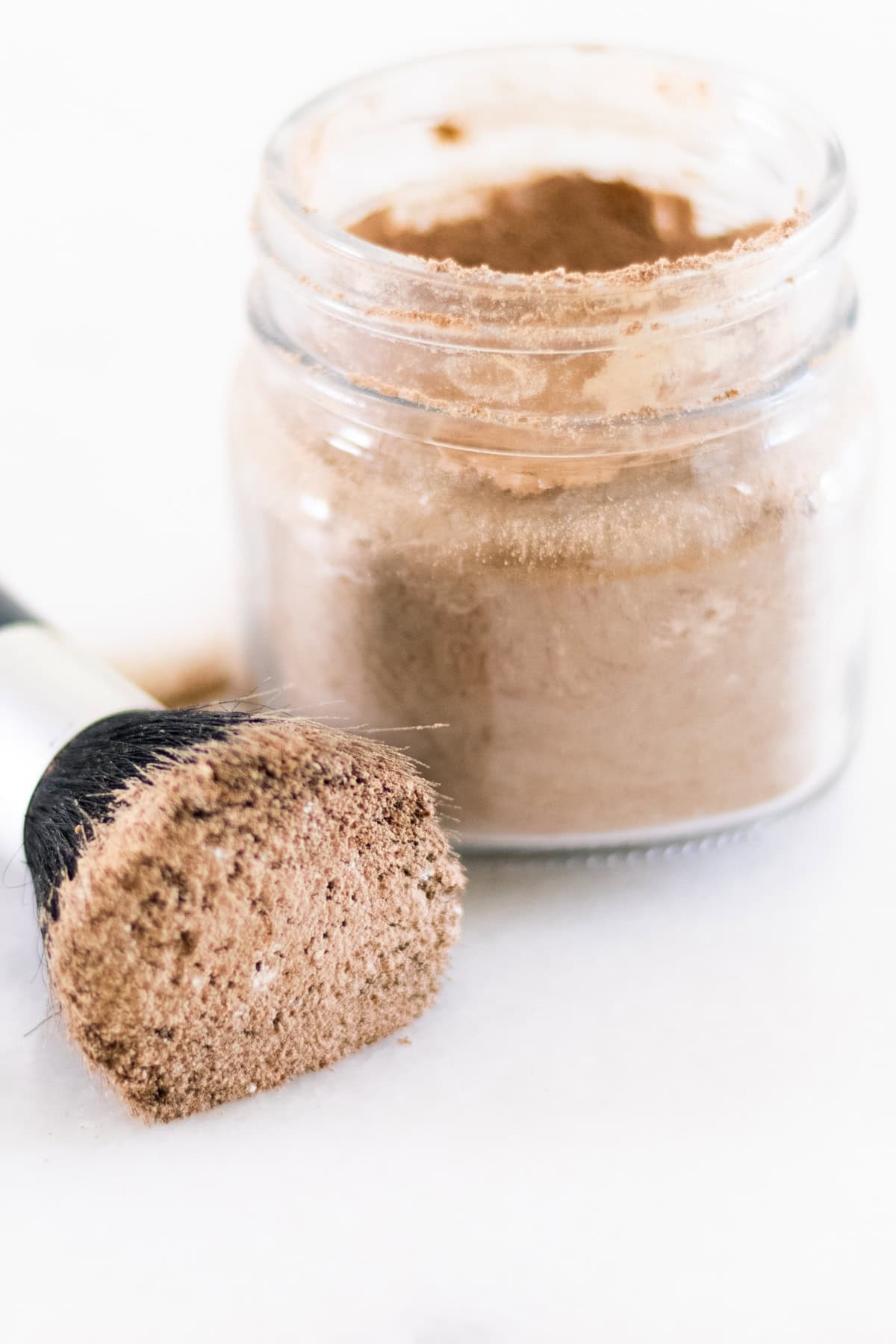 Dry shampoo on a makeup brush with a glass jar of dry shampoo sitting next to it.