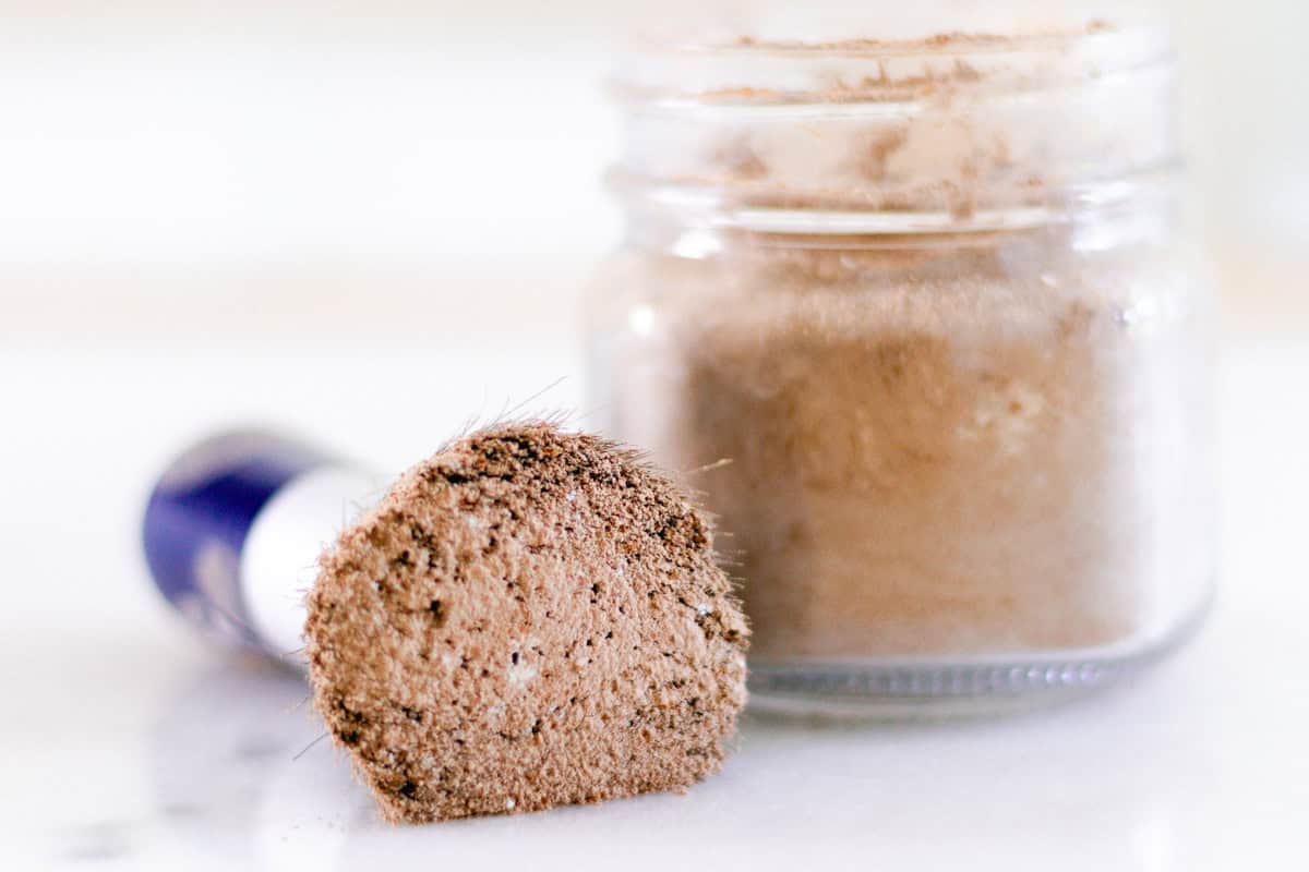 Dry shampoo on a makeup brush with a glass jar of dry shampoo sitting next to it. 