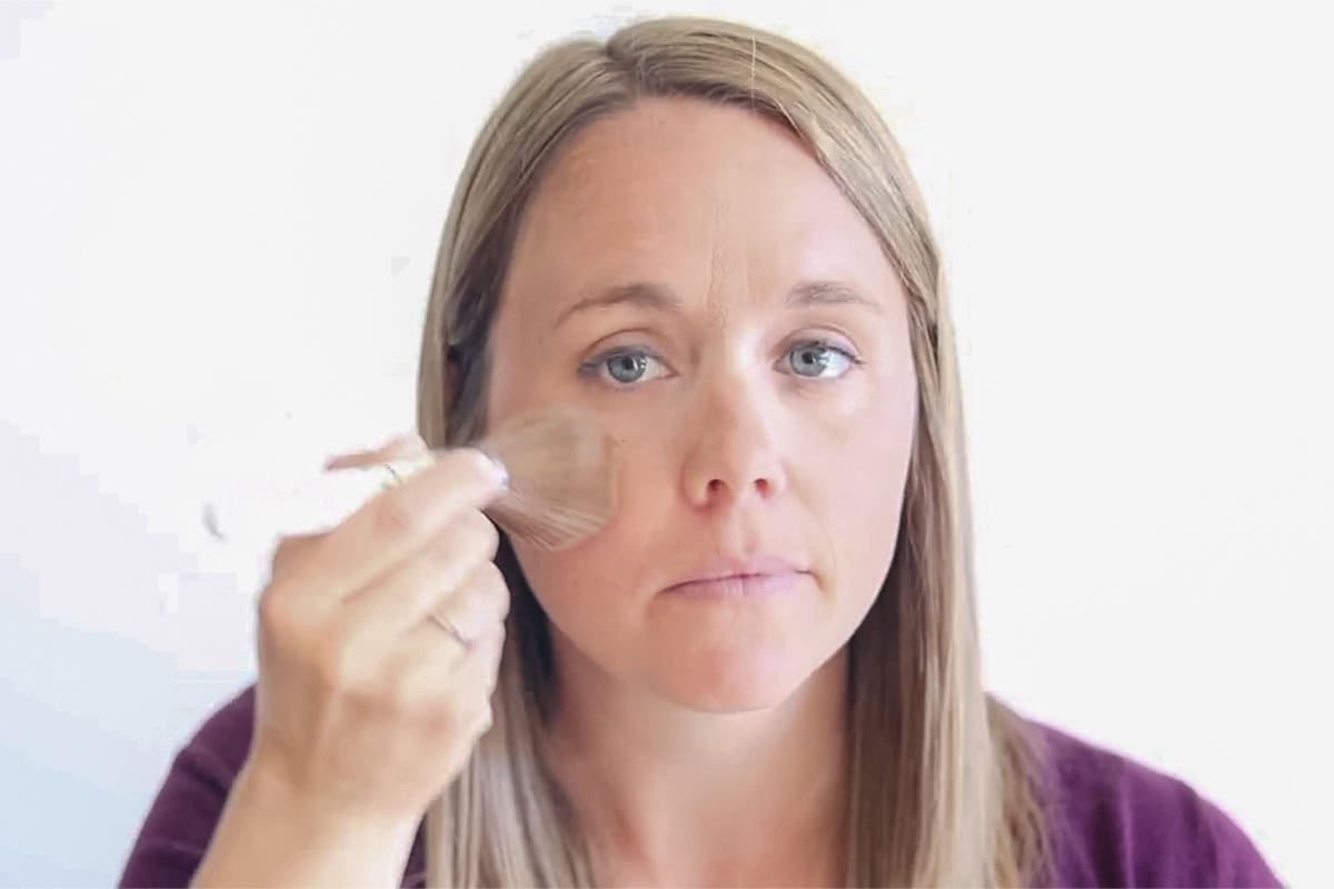 Brushing homemade foundation onto the cheeks with a large brush.