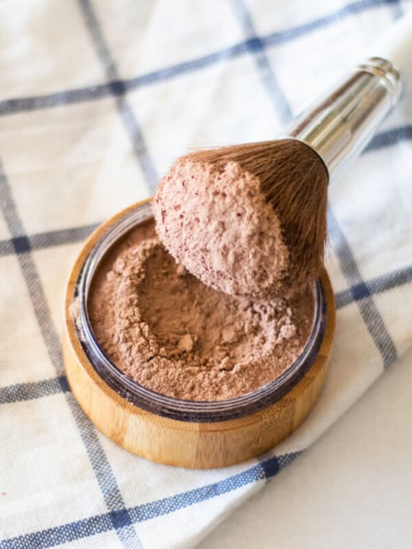 Dipping a makeup brush in a container of homemade foundation.