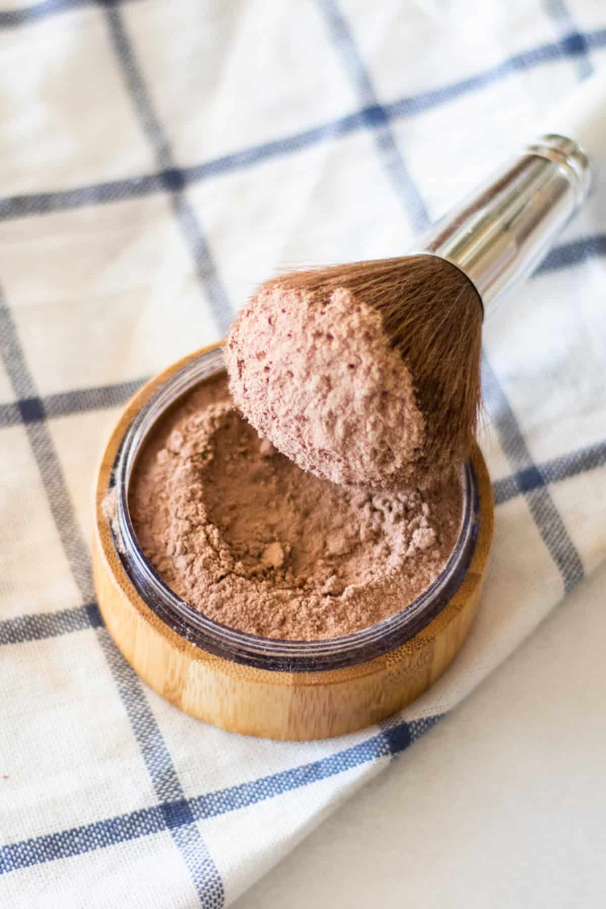 Dipping a makeup brush in a container of homemade foundation.