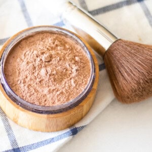 Foundation in a storage container with a makeup brush next to it.