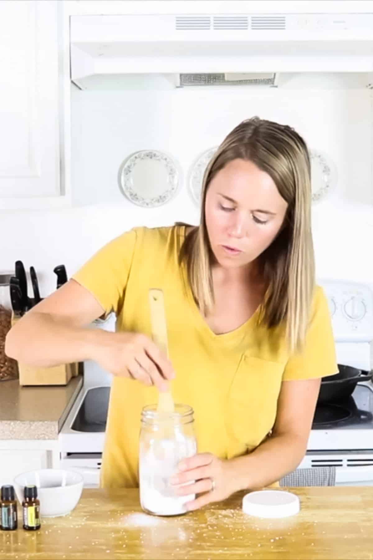 Stirring the ingredients for homemade scent boosters in a jar using a wooden spoon.