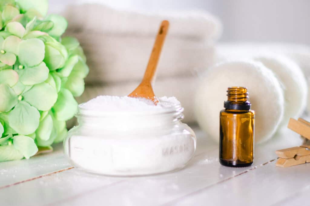 Epsom Salt and baking soda mixture in mason jar on white shiplap with dryer balls and amber colored essential oil bottle.