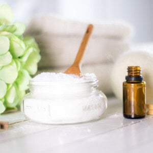 Epsom Salt and baking soda mixture in mason jar on white shiplap with dryer balls and amber colored essential oil bottle.