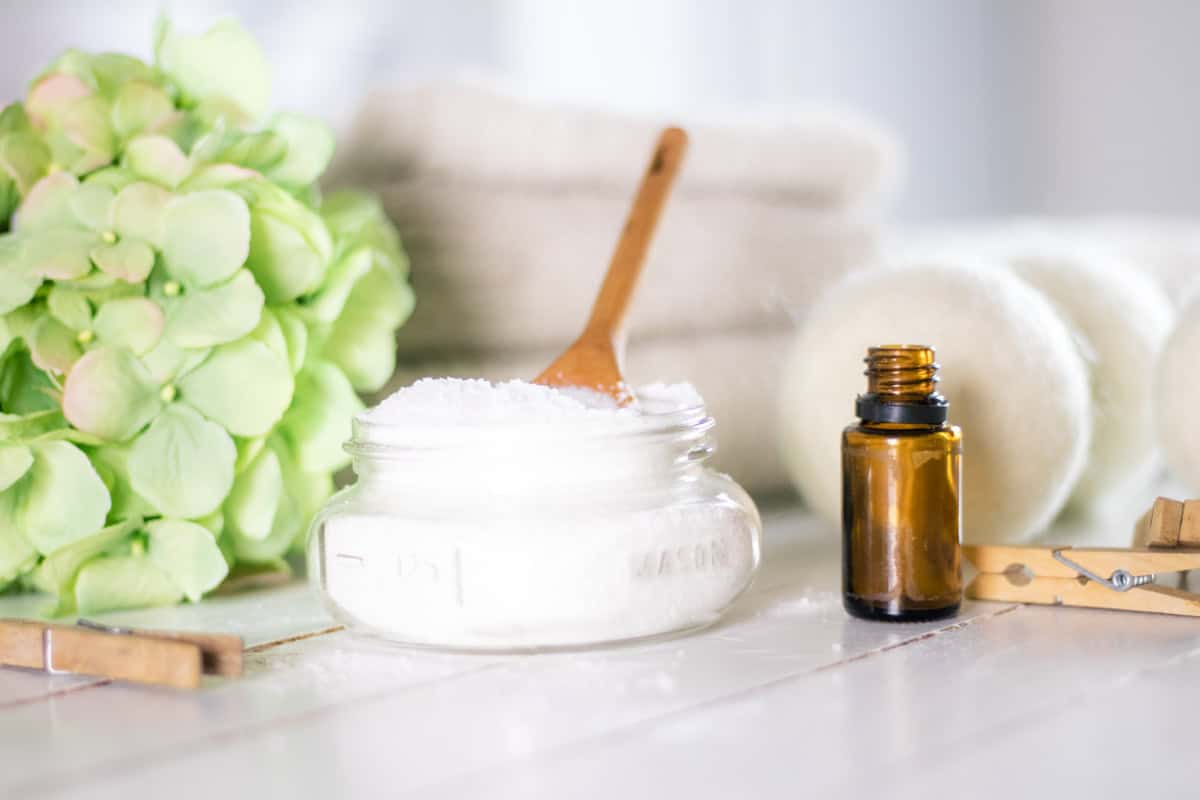 Epsom Salt and baking soda mixture in mason jar on white shiplap with dryer balls and amber colored essential oil bottle.