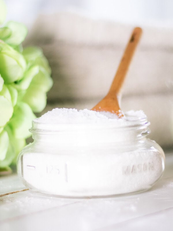 A glass jar filled with homemade laundry scent boosters next to green flowers.