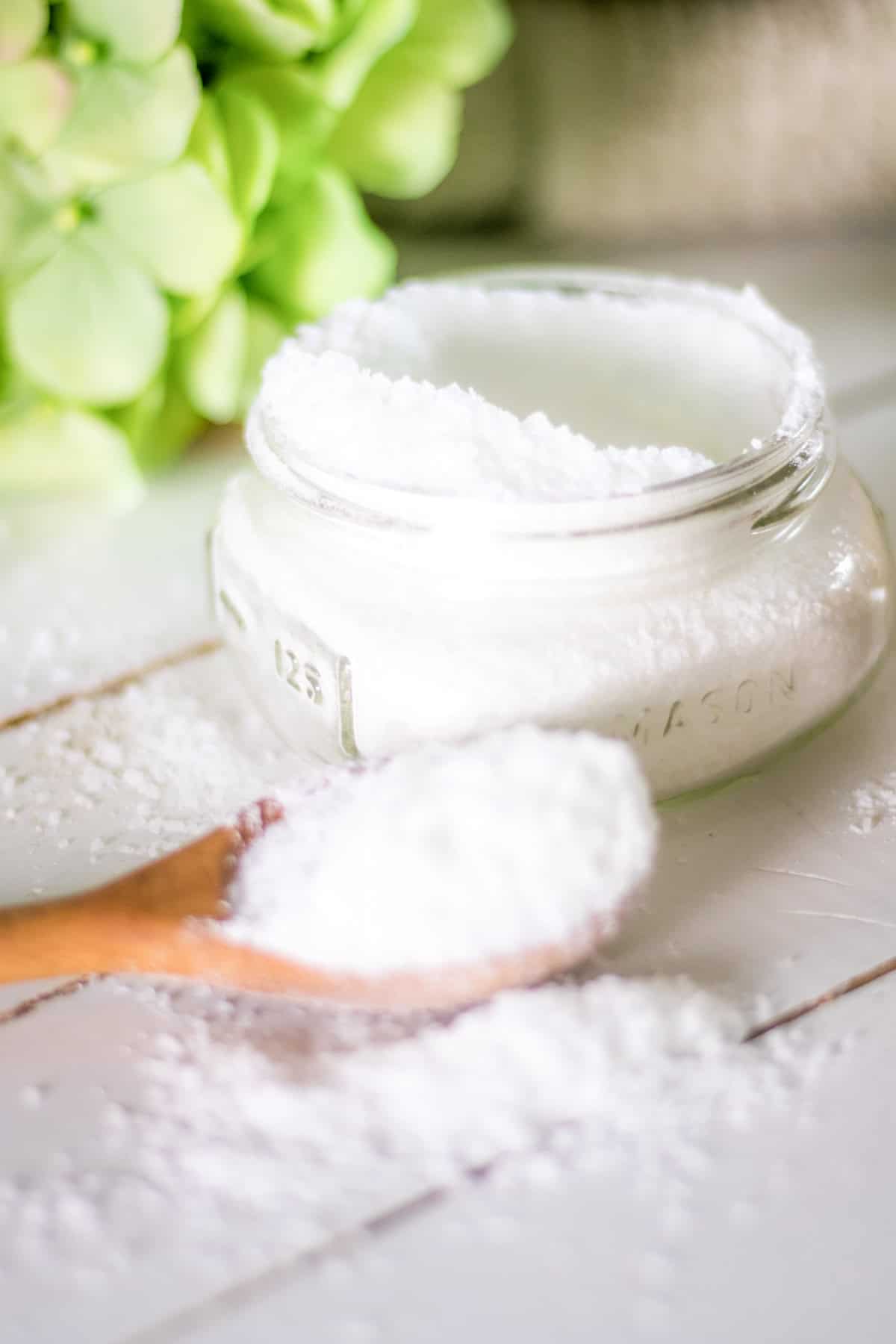 A jar of homemade laundry scent boosters with a spoonful of scent boosters on a white counter. 