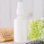 A bottle of leave-in conditioner next to dried flowers and a hair brush.