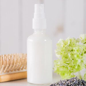 A bottle of leave-in conditioner next to dried flowers and a hair brush.