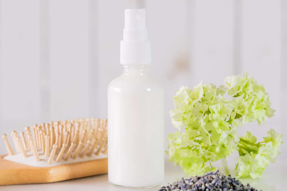 A bottle of leave-in conditioner next to dried flowers and a hair brush.