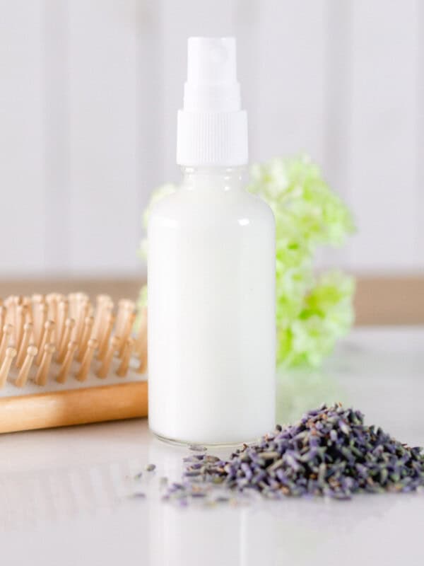 A bottle of leave-in conditioner next to dried lavender and a hair brush.