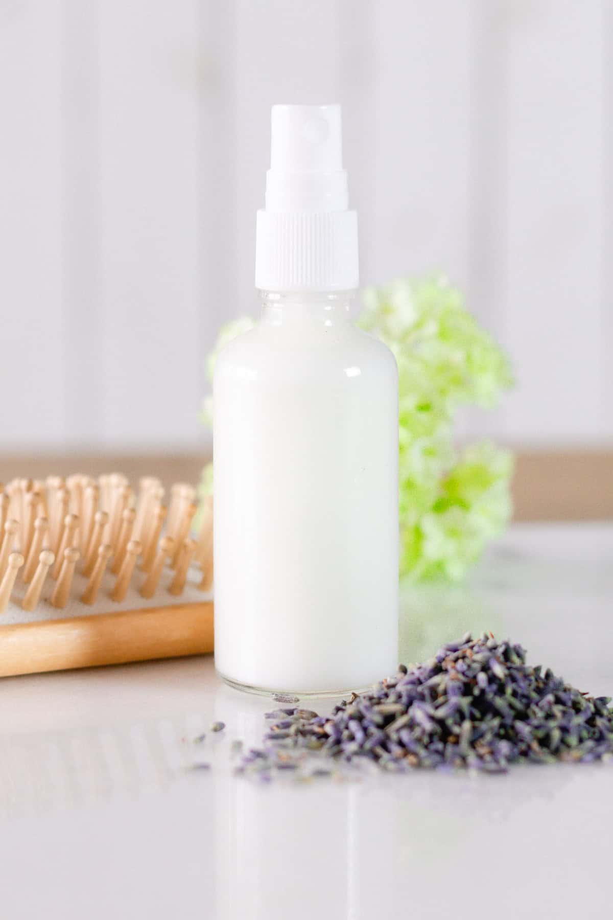 A bottle of leave-in conditioner next to dried lavender and a hair brush.