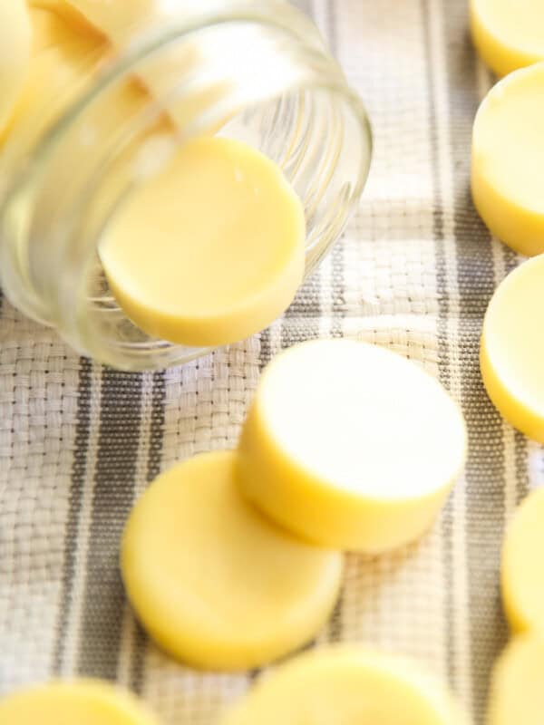 Homemade lotion bars spilled out of a large mouth mason jar onto a white and grey tea towel.