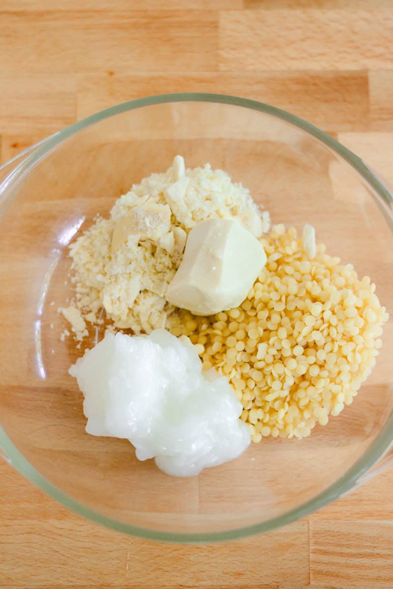 A glass bowl with lotion bar ingredients sitting on a wooden table.