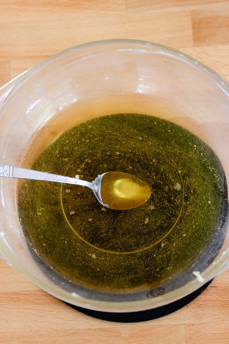 Lotion bar ingredients in a glass bowl, completely melted with a spoon in the bowl.