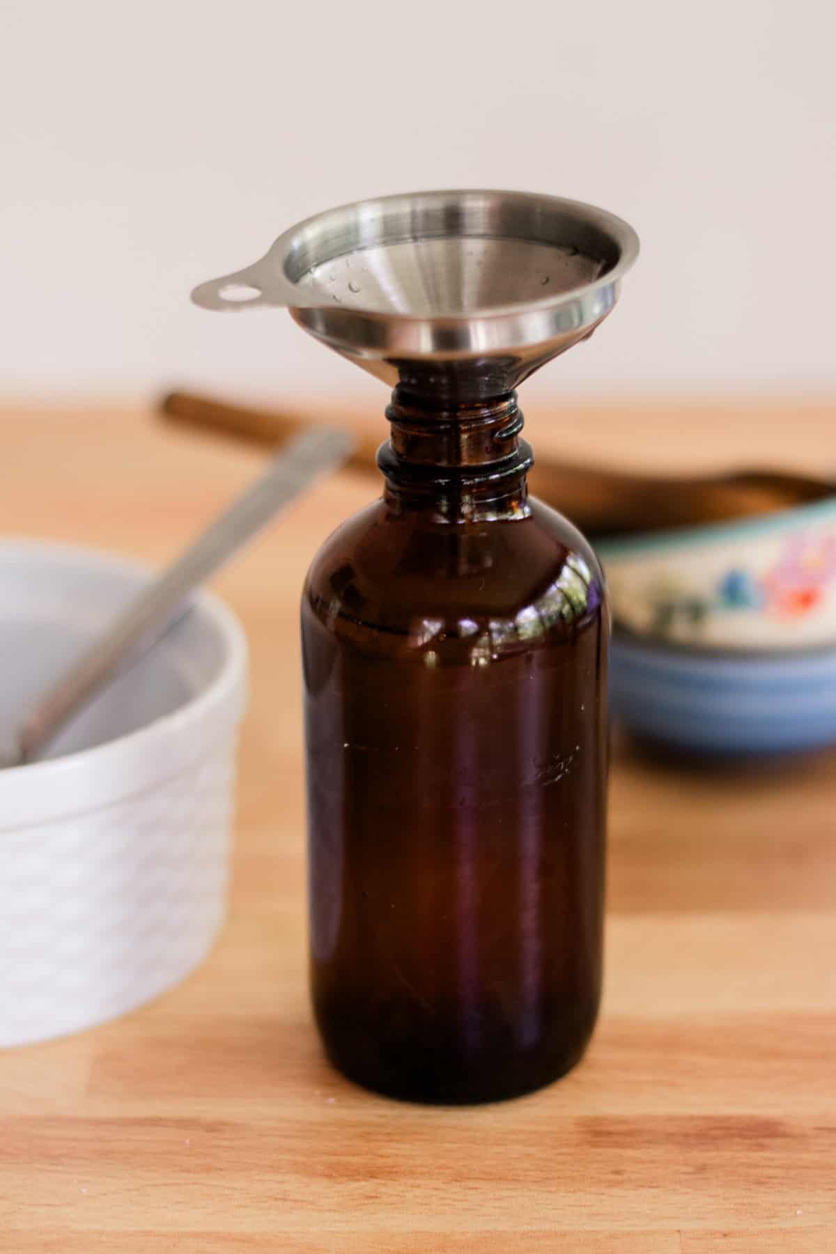 An amber glass bottle with a small metal funnel in the top.