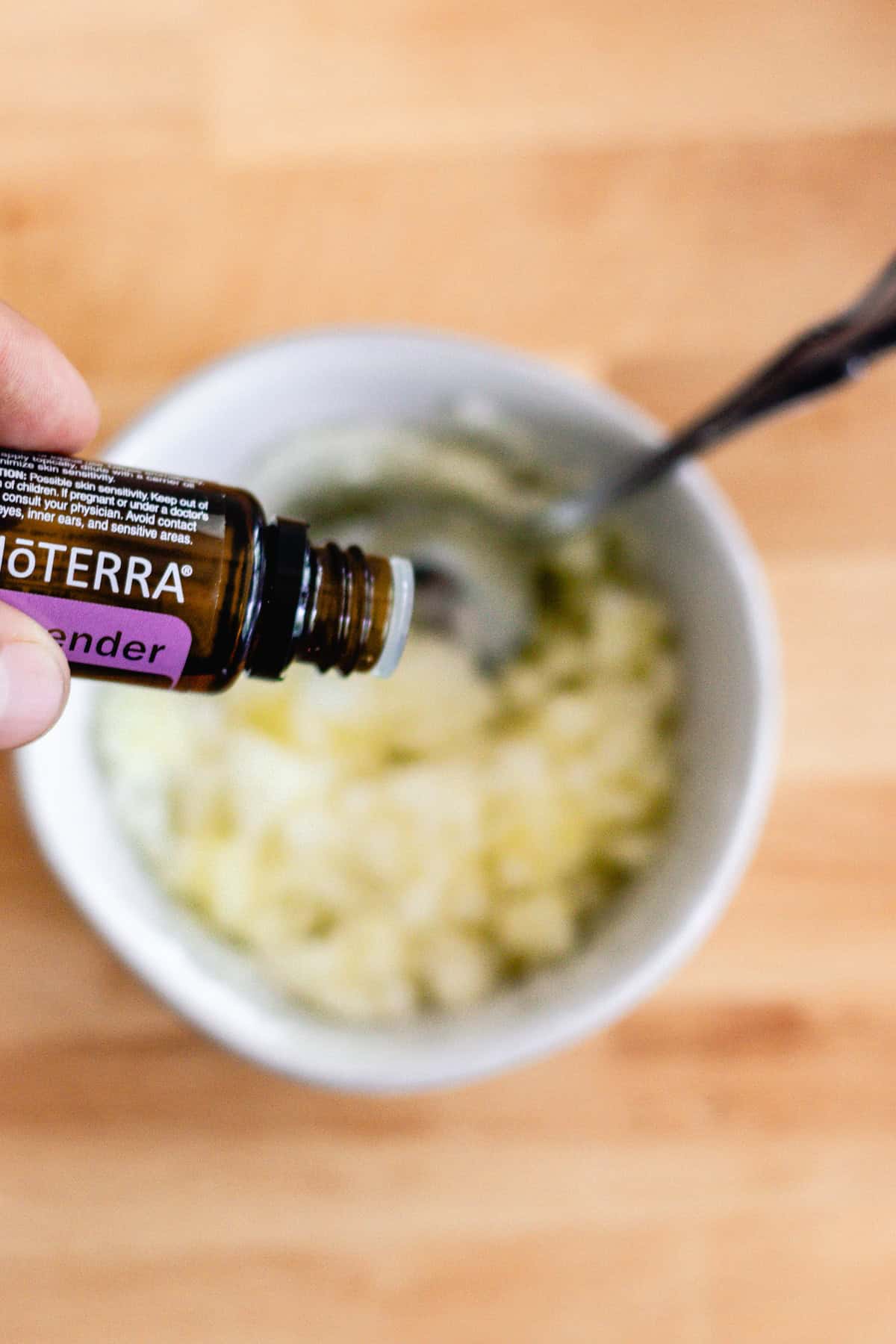 Dropping lavender essential oil into a bowl of mixed olive oil and sugar. 