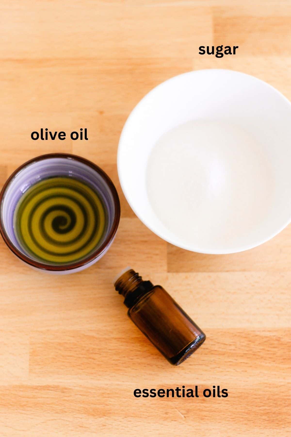 Ingredients laid out for a homemade sugar scrub. Olive oil, sugar, and a small bottle of essential oil. 