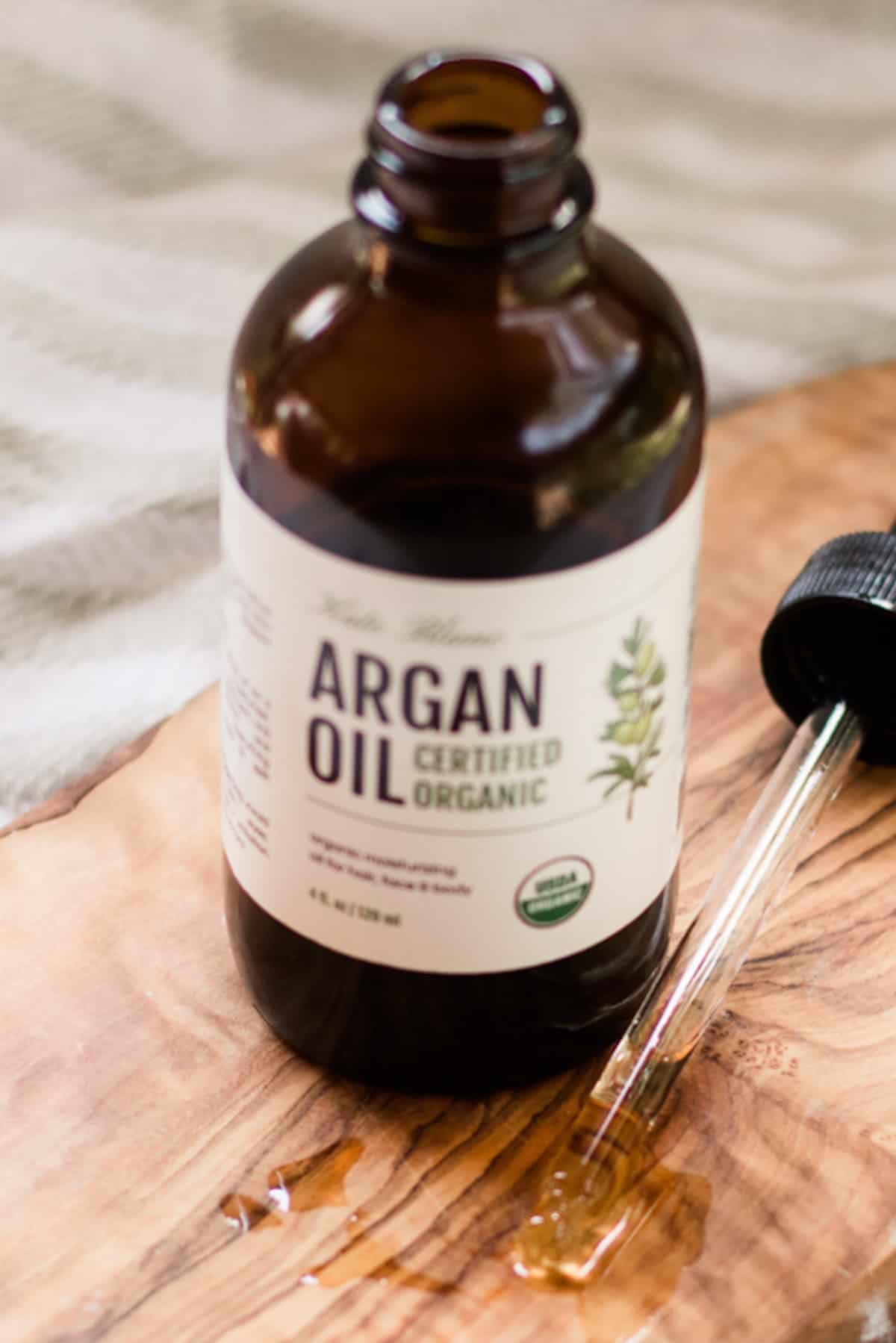 Argan bottle open with dropper of argan oil in front of it.