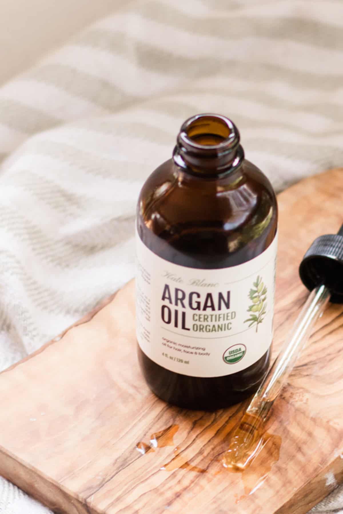 Amber glass bottle of argan oil on wooden board. 