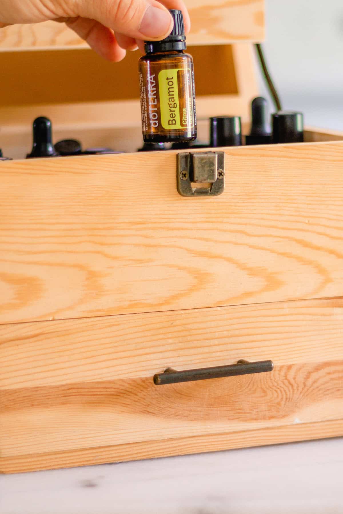Picking up a bergamot oil out of a wooden essential oil storage box. 