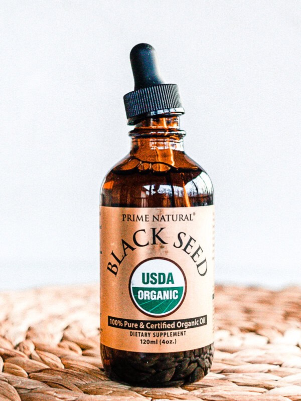 Dropper bottle of black seed oil on a wicker table top.