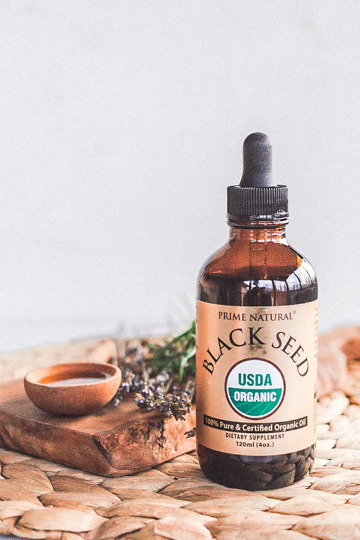 Black seed oil is in a small bottle with a wooden spoon next to it, and lavender sprigs are in the background. 