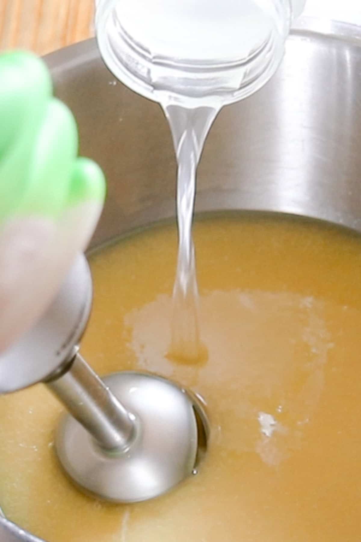 Mixing with an immersion blender while pouring the lye and water mixture into the bowl.