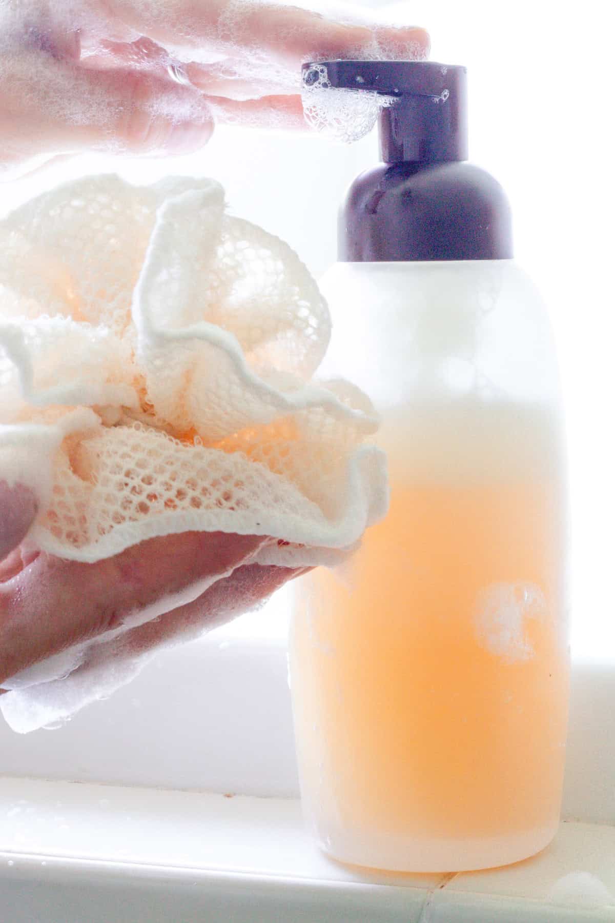 Squirting natural body wash out of a bottle onto a loofah.