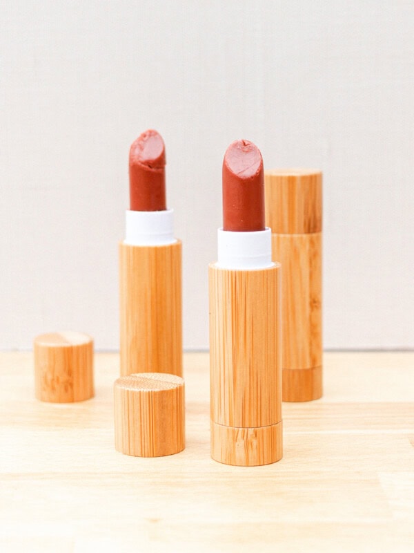 2 tubes of lipstick sitting on a wooden countertop with a closed tube of homemade lipstick in the background.