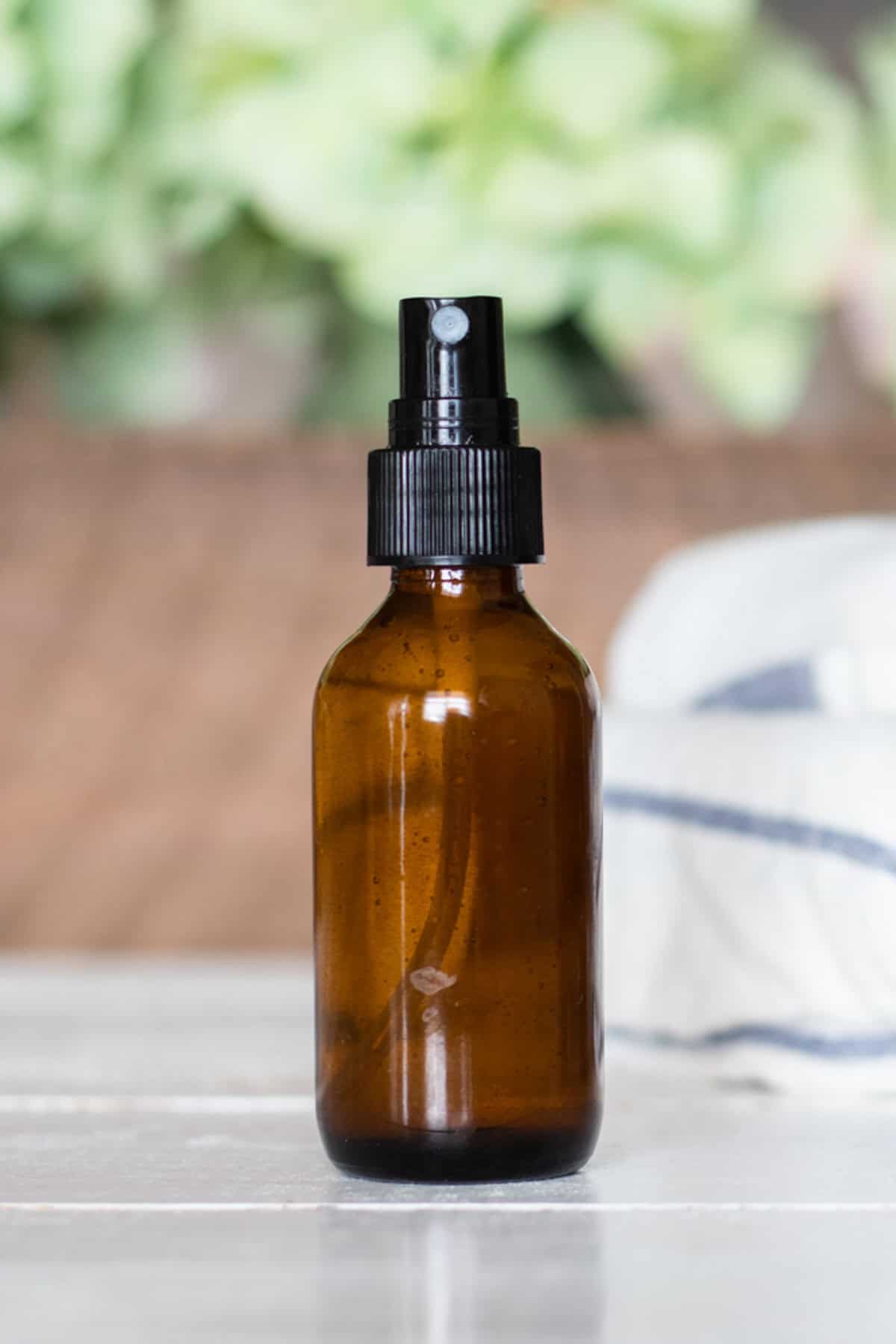 An amber bottle of spray deodorant with green flowers in the background.