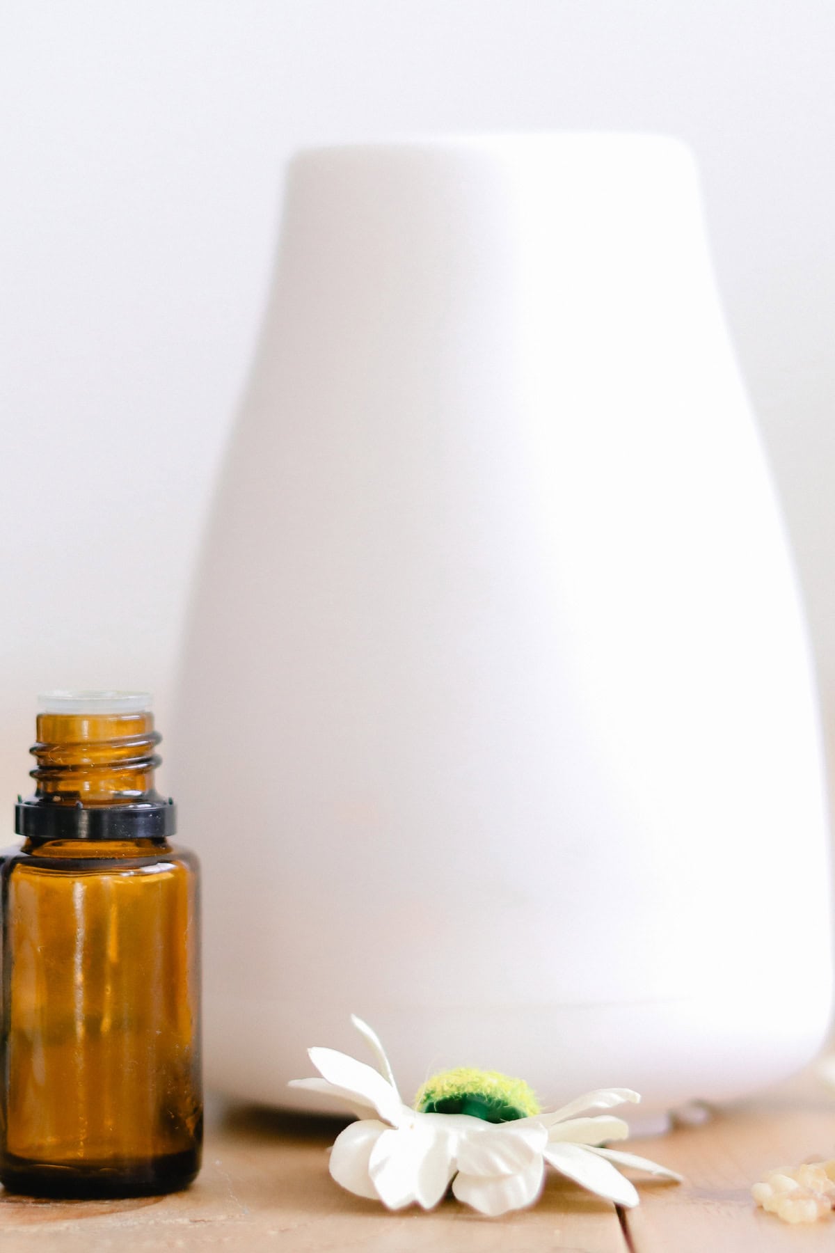A minimalist essential oil diffuser with a delicate white flower, and an amber-colored essential oil bottle on a wooden surface.
