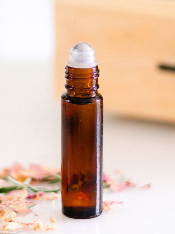 An amber roller bottle with flower petals scattered around it.