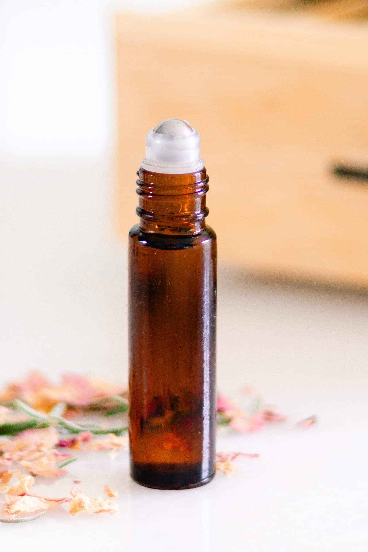 An amber roller bottle with flower petals scattered around it.