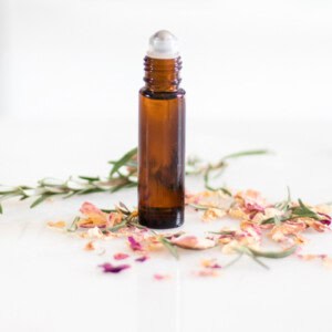 An amber roller bottle with flower petals scattered around it.