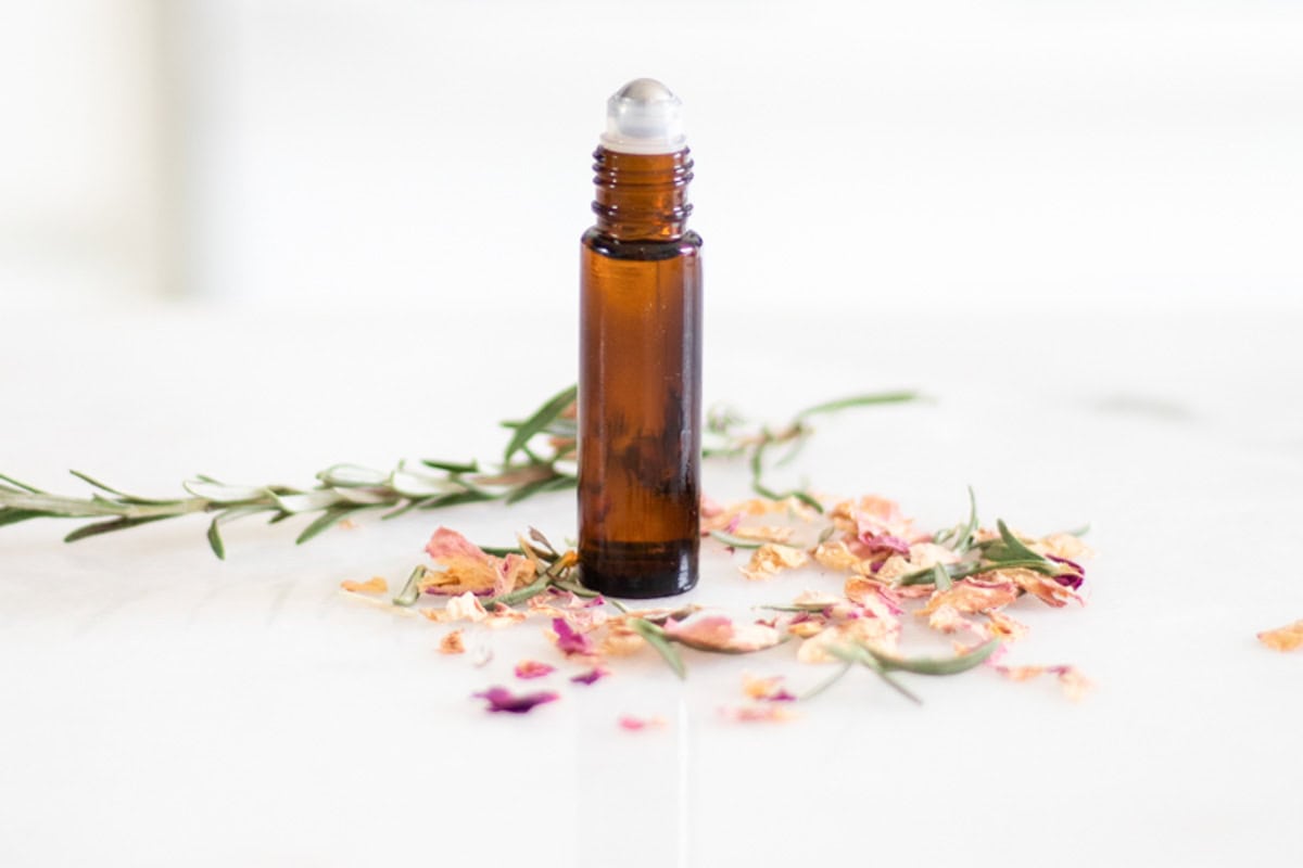 An amber roller bottle with flower petals scattered around it.