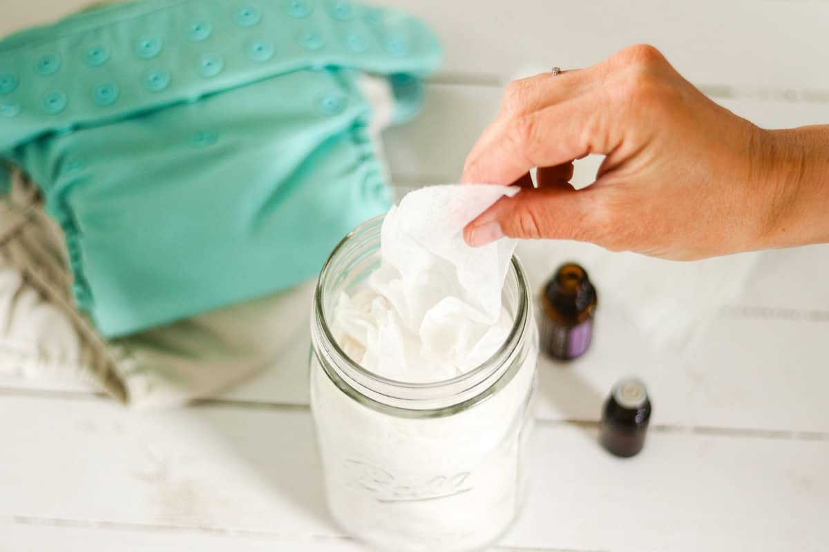 Pulling a homemade natural baby wipe out of a mason jar next to a cloth diaper.