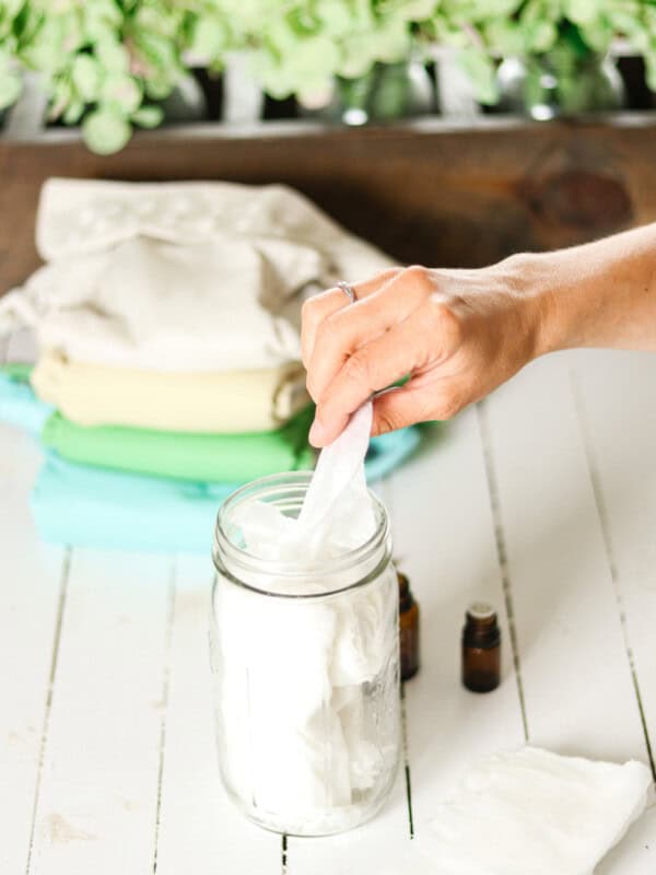 Pulling a homemade natural baby wipe out of a mason jar next to a cloth diaper.