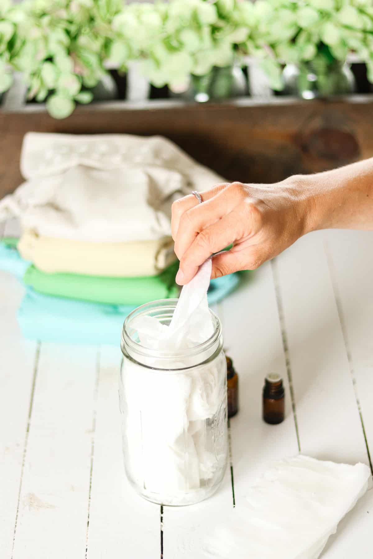 Pulling a homemade natural baby wipe out of a mason jar next to a cloth diaper.